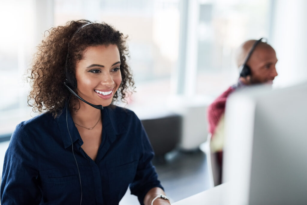 African American CSR wearing a phone headset smiling while looking at her computer