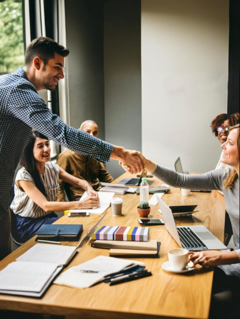 An IT Hiring Manager shaking hands with a candidate at the end of the interview while three other members of the interview panel looks on.
